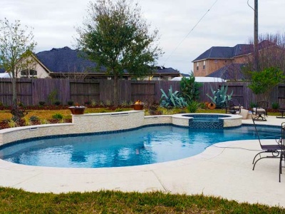 Freeform Pool and Spa with Glass Tiles, Raised Walls, Travertine Scuppers, Natural Gas Fire Bowls in Riverstone